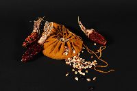 Three ears of reddish corn set around a leather bag that contains dried corn kernels.